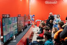 A lively group enjoys gaming at a Nintendo event in Zagreb, featuring multiple screens and vibrant atmosphere.