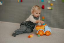 Cute toddler playing with a colorful toy truck indoors surrounded by building blocks.