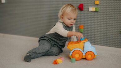 Cute toddler playing with a colorful toy truck indoors surrounded by building blocks.