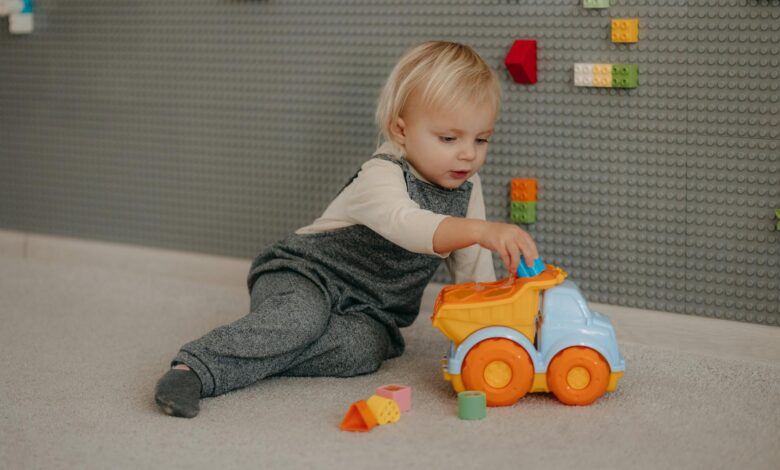 Cute toddler playing with a colorful toy truck indoors surrounded by building blocks.
