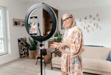 Elderly woman filming social media video with smartphone and ring light in modern living room.