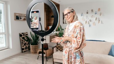 Elderly woman filming social media video with smartphone and ring light in modern living room.