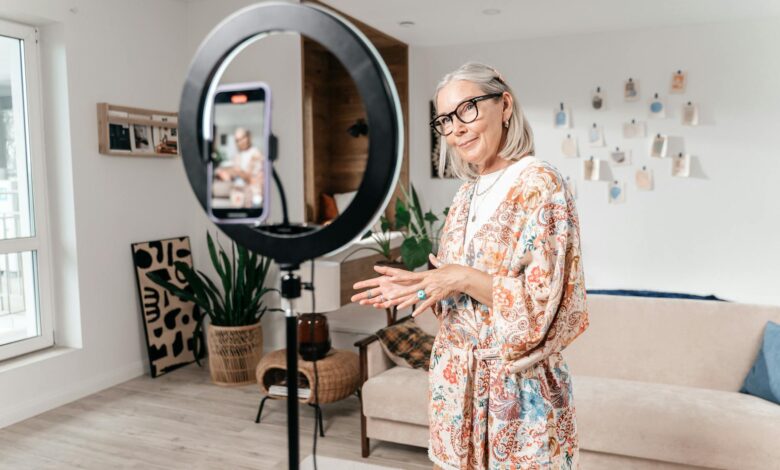 Elderly woman filming social media video with smartphone and ring light in modern living room.