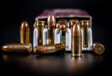 Detailed close-up of copper ammunition bullets in a cardboard box on black background.