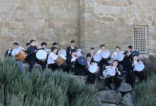 Group of boys playing drums against a historic stone wall outdoors.
