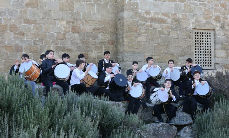 Group of boys playing drums against a historic stone wall outdoors.