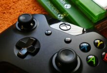 Xbox controller close-up with game cases on orange background.