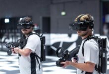 Two men playing a virtual reality game indoors in Paris, using VR headsets and gear.