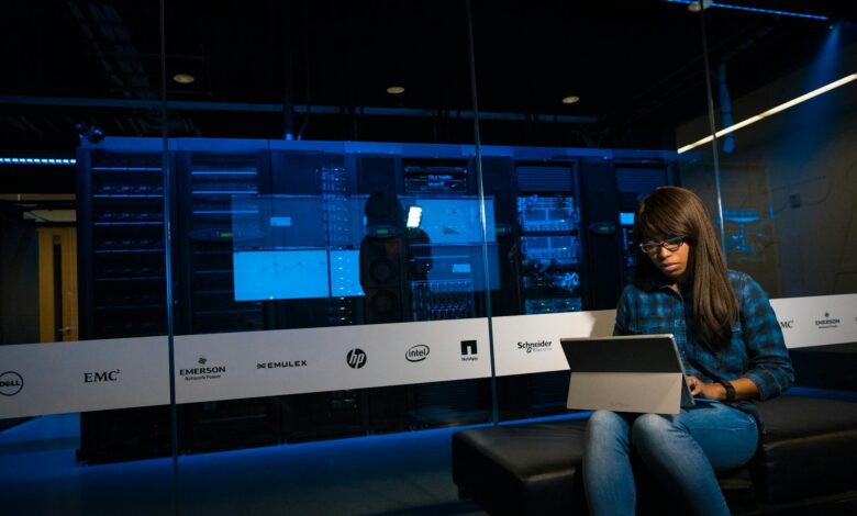 Woman using a laptop in a server room, showcasing modern technology and work environment.