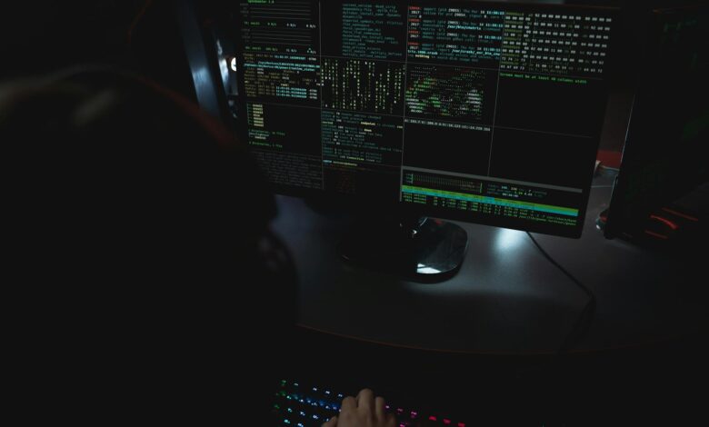 Dark room setup with code displayed on PC monitors highlighting cybersecurity themes.