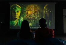 Two people sitting indoors gaming on a large projector screen, enjoying a video game session.