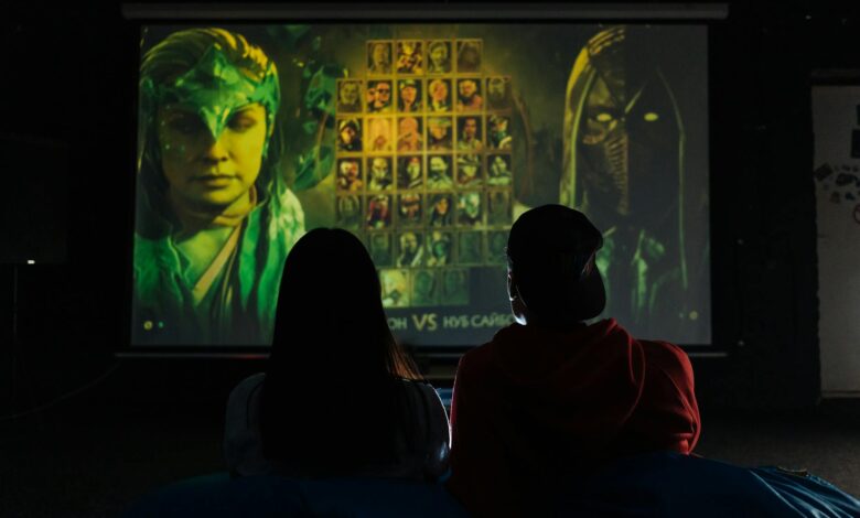 Two people sitting indoors gaming on a large projector screen, enjoying a video game session.