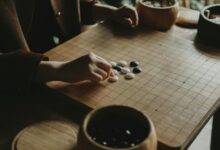A person playing Go, arranging black and white stones on a wooden board indoors.