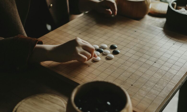 A person playing Go, arranging black and white stones on a wooden board indoors.