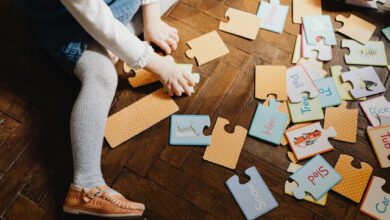 Child engaging with educational puzzle pieces on wooden floor indoors, fostering learning and play.