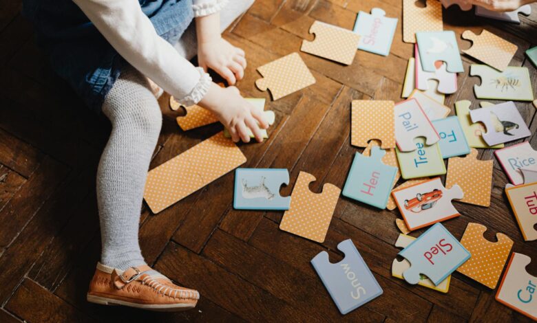 Child engaging with educational puzzle pieces on wooden floor indoors, fostering learning and play.