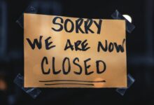 A handwritten sign with 'Sorry We Are Now Closed' in a dark window setting.