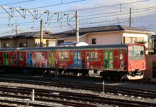 Vibrant train with cartoon designs in Japanese neighborhood under clear skies.