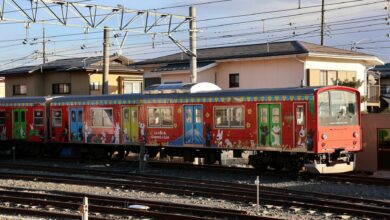 Vibrant train with cartoon designs in Japanese neighborhood under clear skies.