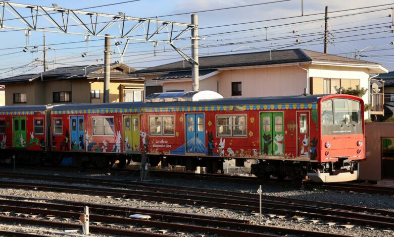 Vibrant train with cartoon designs in Japanese neighborhood under clear skies.