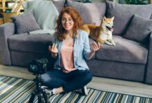 Redhead woman recording a video at home with her Shiba Inu dog on the couch.