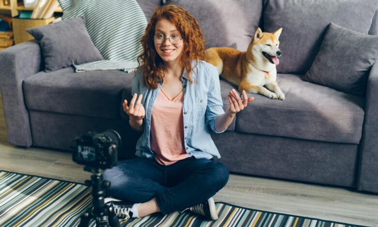 Redhead woman recording a video at home with her Shiba Inu dog on the couch.