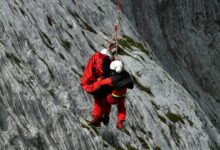 Two rescuers in action on a mountain, showcasing teamwork and safety in a daring lift.