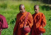 Buddhist monks in vibrant robes walking outdoors, holding alms bowls during a spiritual procession.