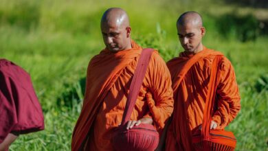 Buddhist monks in vibrant robes walking outdoors, holding alms bowls during a spiritual procession.