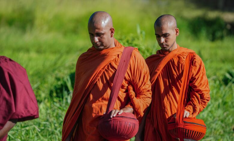 Buddhist monks in vibrant robes walking outdoors, holding alms bowls during a spiritual procession.