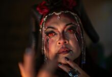 A woman in demon makeup with red eyes and horns, exuding a mystical aura.