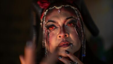 A woman in demon makeup with red eyes and horns, exuding a mystical aura.