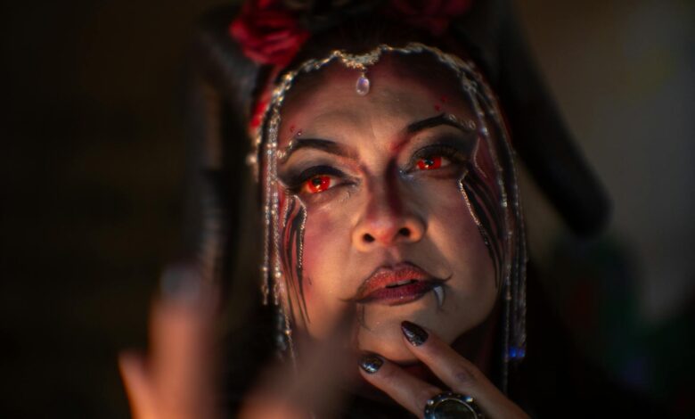 A woman in demon makeup with red eyes and horns, exuding a mystical aura.