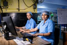 Two female workers at a textile factory operating computers in an industrial setting.