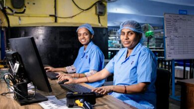 Two female workers at a textile factory operating computers in an industrial setting.
