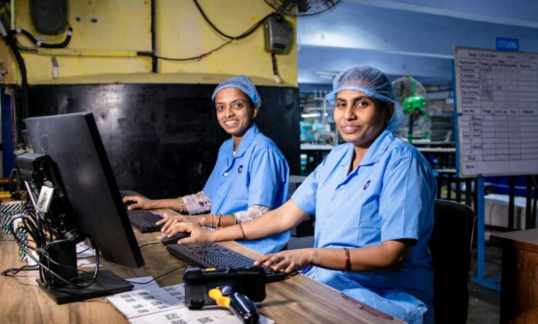 Two female workers at a textile factory operating computers in an industrial setting.