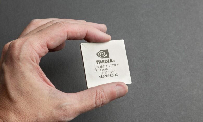 A close-up view of a person holding an Nvidia chip with a gray background.