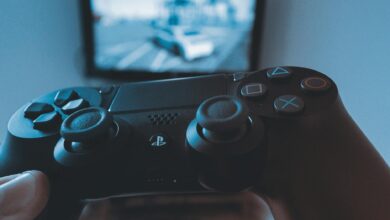 A hand holding a wireless game controller in front of a blurry screen, capturing the gaming experience.
