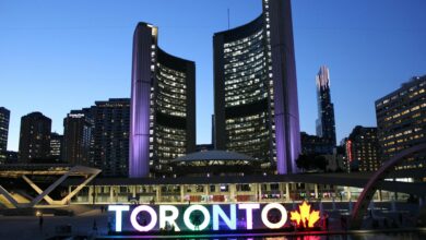 Toronto City Hall illuminated at twilight with colorful Toronto sign in the foreground.