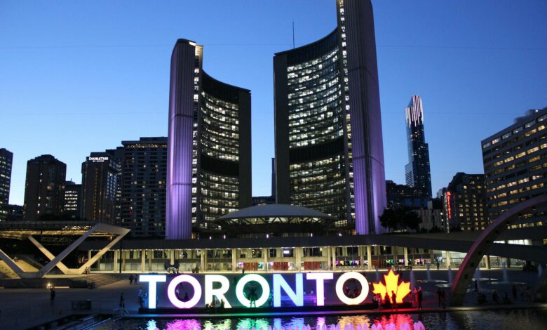 Toronto City Hall illuminated at twilight with colorful Toronto sign in the foreground.