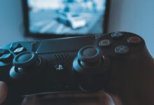 A hand holding a wireless game controller in front of a blurry screen, capturing the gaming experience.