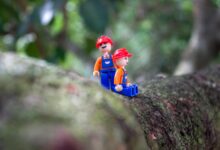 Two plastic toy figures resembling construction workers on a tree branch in a natural setting.