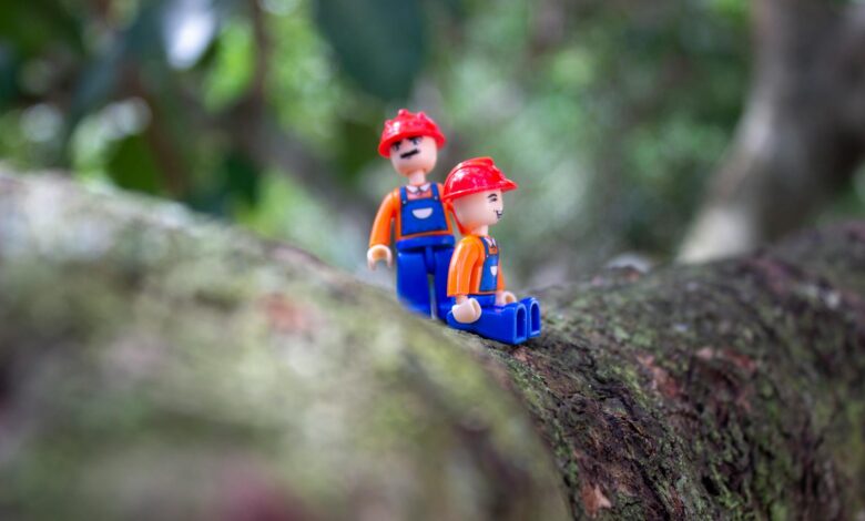 Two plastic toy figures resembling construction workers on a tree branch in a natural setting.
