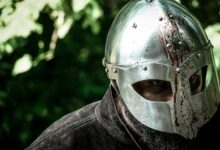 Close-up of a knight in a blood-stained helmet, evoking medieval combat.