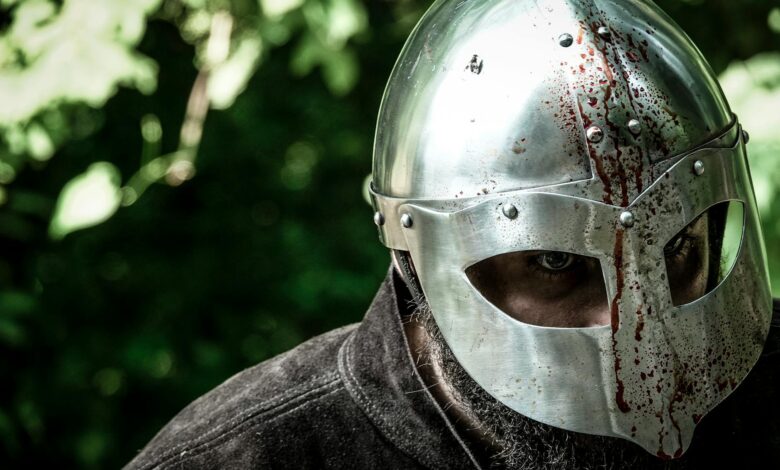 Close-up of a knight in a blood-stained helmet, evoking medieval combat.