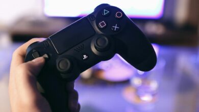 Person holding a gaming controller, blurred screen in background.