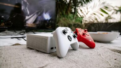White and red game controllers on carpet with TV in the background, set outdoors.