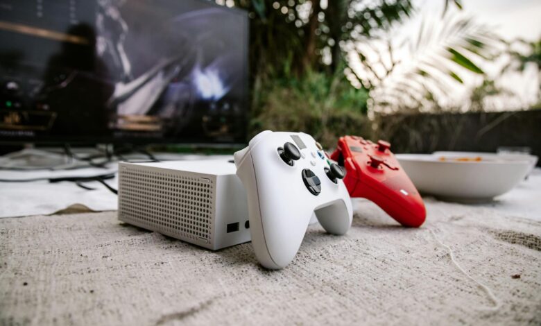 White and red game controllers on carpet with TV in the background, set outdoors.