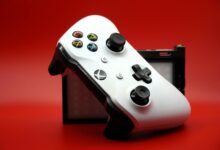 Close-up of a white gaming controller with black buttons against a vivid red backdrop.
