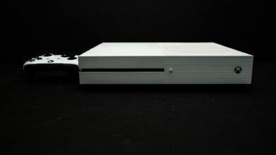 Close-up of a white gaming console with a black controller on a dark background.